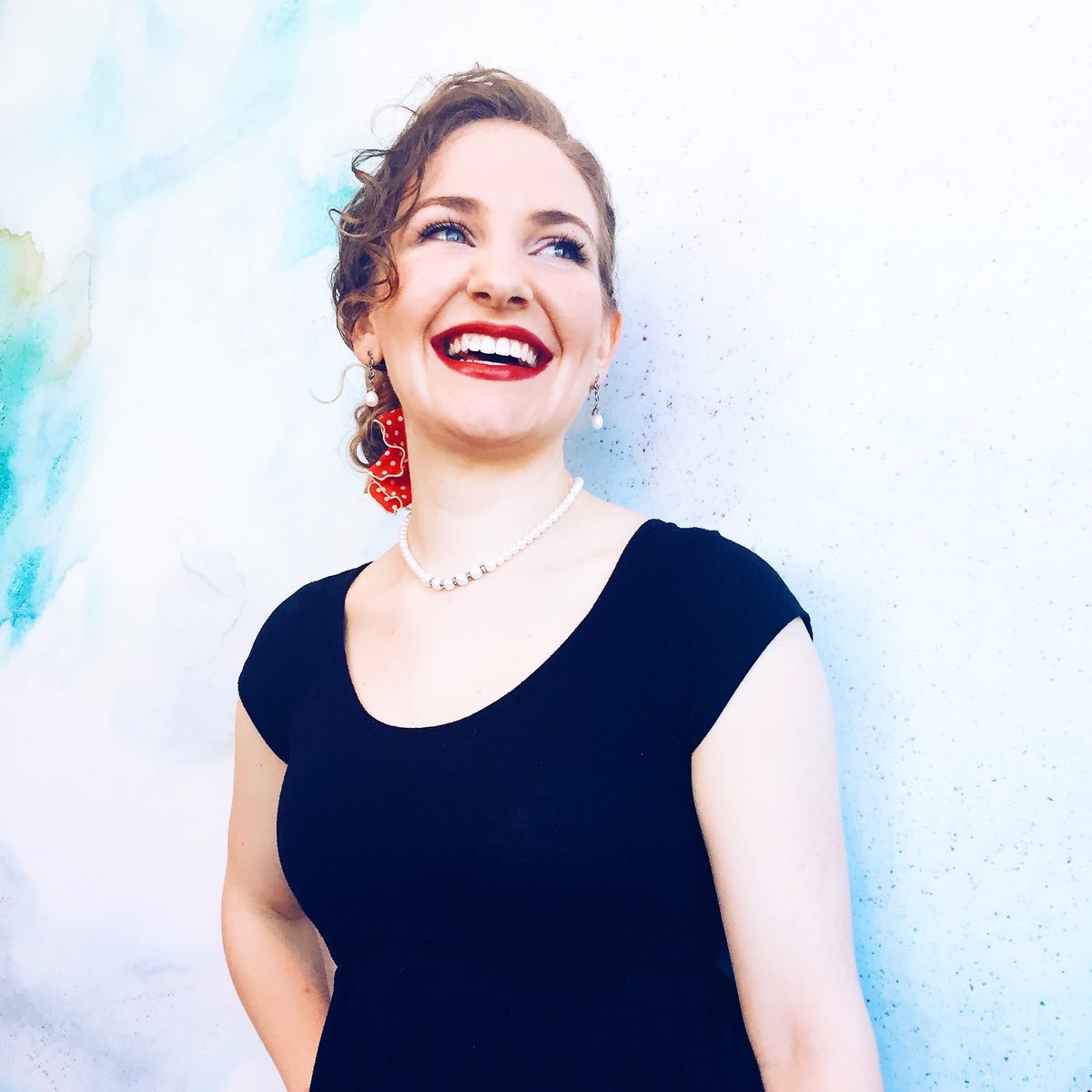 Grace laughing in a black dress with a red polka-dot hair scarf and pearls.