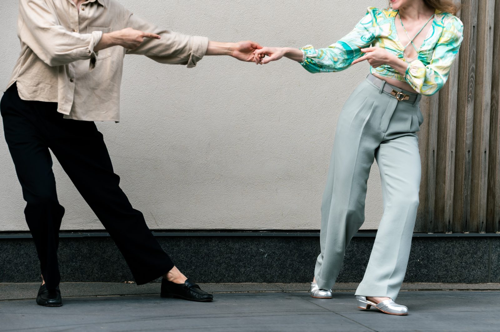 Two dancers stretched into a playful send-out against a city wall.